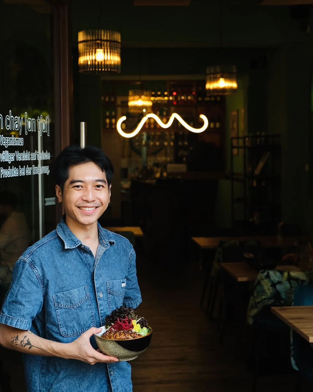 Gastgeber von Ăn Chay hält eine bunte vegane Bowl vor dem begrünten Gastraum